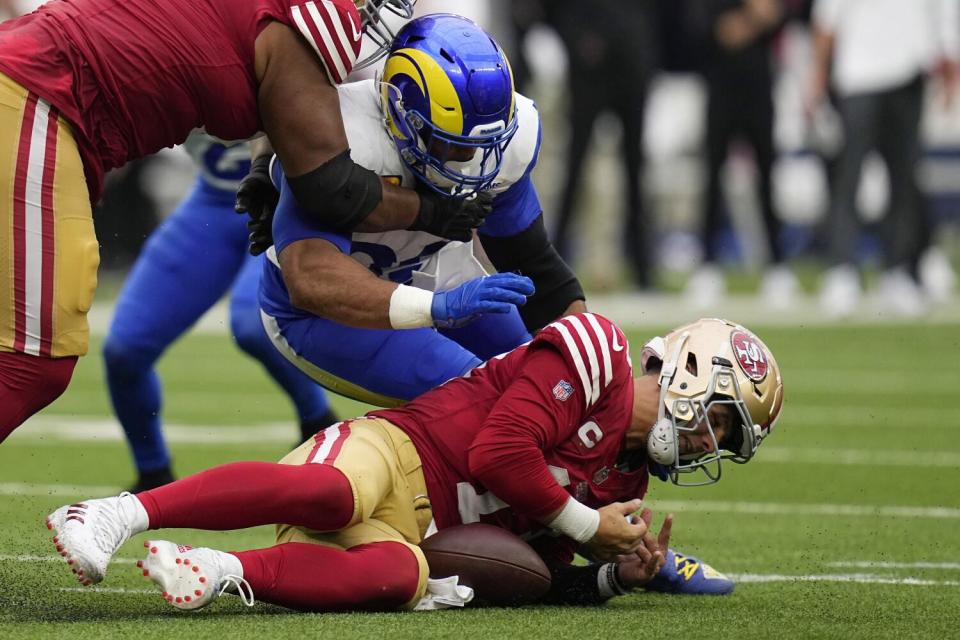 San Francisco 49ers quarterback Brock Purdy falls on a fumble as the Rams' Aaron Donald pursues.