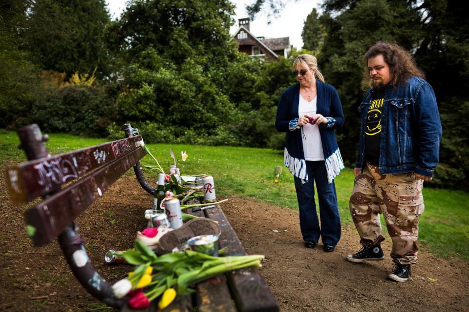 Several hundred yards from the home where Nirvana's Kurt Cobain killed himself in 1994, background, fans of the late lead singer such as Beau Allen, 27, right, and his mother, Bobbi Binder, center right, visit a bench loaded with offerings of flowers, unopened beers and handwritten notes on the 20th anniversary of Cobain's death, Saturday, April 5, 2014, at Viretta Park in Seattle, Wash. Allen also visited the site on the tenth anniversary of the singer's death, and has been a fan of Nirvana since age six. On April 10, 2014, Nirvana will be inducted into the Rock and Roll Hall of Fame. (AP Photo/seattlepi.com, Jordan Stead) STAND ALONE PHOTO. MAGS OUT; NO SALES; SEATTLE TIMES OUT; MANDATORY CREDIT; TV OUT