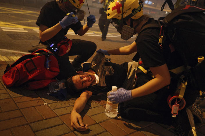 FILE - In this file photo taken Sunday, July 21, 2019, medical workers help a protester in pain from tear gas fired by policemen on a street in Hong Kong. The former British colony of Hong Kong was returned to China in 1997 under a “one country, two systems” concept that gives the city a fair degree of autonomy over its affairs, but China may intervene to quell protests now in their seventh week. (AP Photo/Bobby Yip, File)