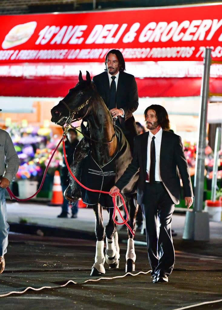 Keanu Reeves riding a horse being led by his stunt double on the set of John Wick 3