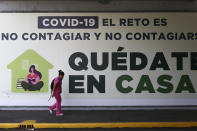 FILE - In this Tuesday, March 31, 2020 file photo, a woman walks past a sign in Mexico City that translates in English to, "COVID=19. The challenge is not to get it and not spread it. Stay home." On Friday, May 22, 2020, The Associated Press reported on stories circulating online incorrectly asserting the letters in COVID-19 stand for certificate of vaccination identification and 19 stands for AI, artificial intelligence. COVID-19 stands for “coronavirus disease 2019,” according to the World Health Organization, which named it in February. In selecting a name, the WHO avoided anything that sounded similar to any geographical location, animal, individual or group of people, according to WHO director-general Tedros Adhanom Ghebreyesus. The name also had to be related to the disease and pronounceable. (AP Photo/Eduardo Verdugo)