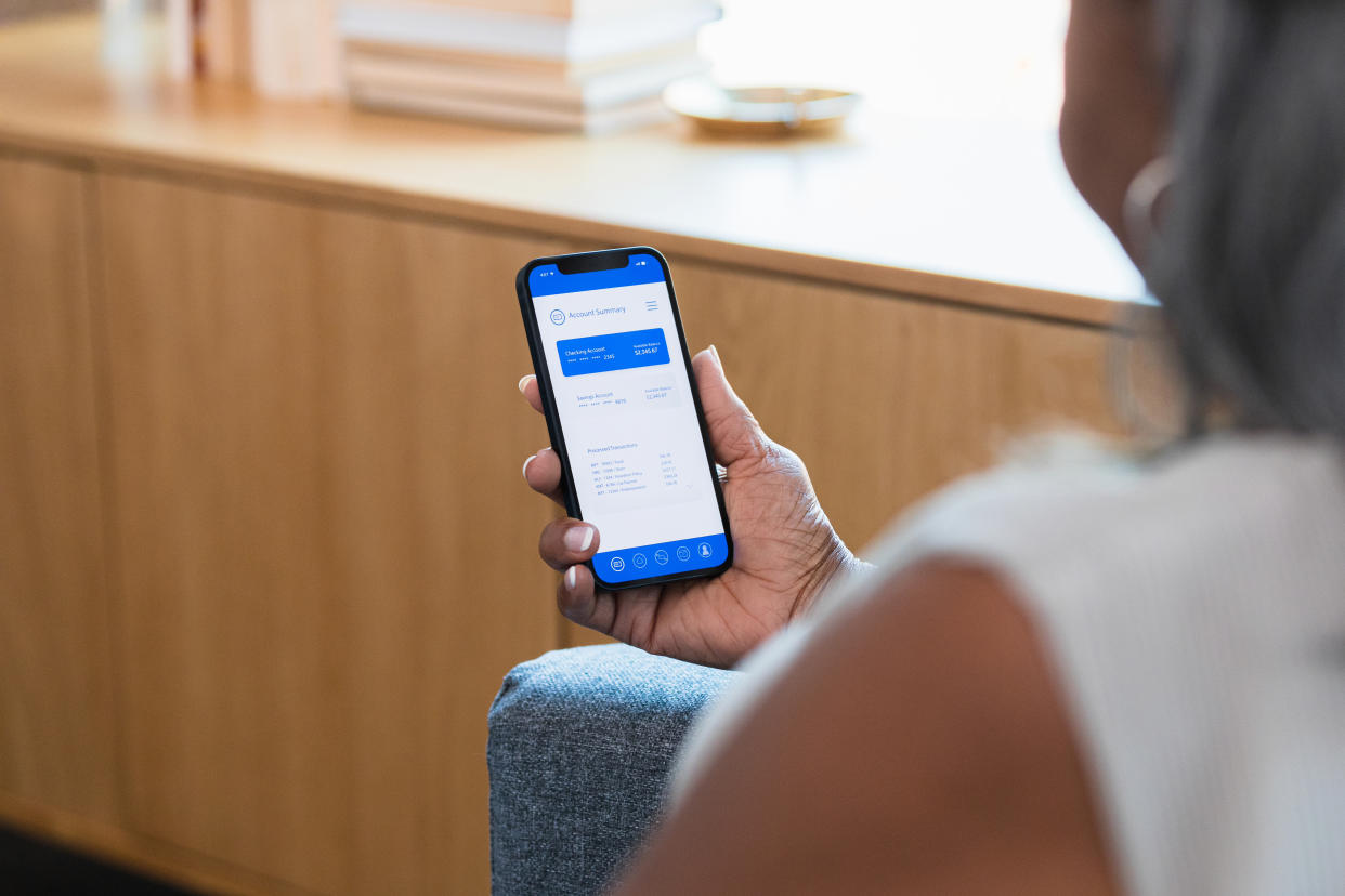 Sitting at home in her living room, the unrecognizable senior adult woman uses an online banking app on her smart phone.