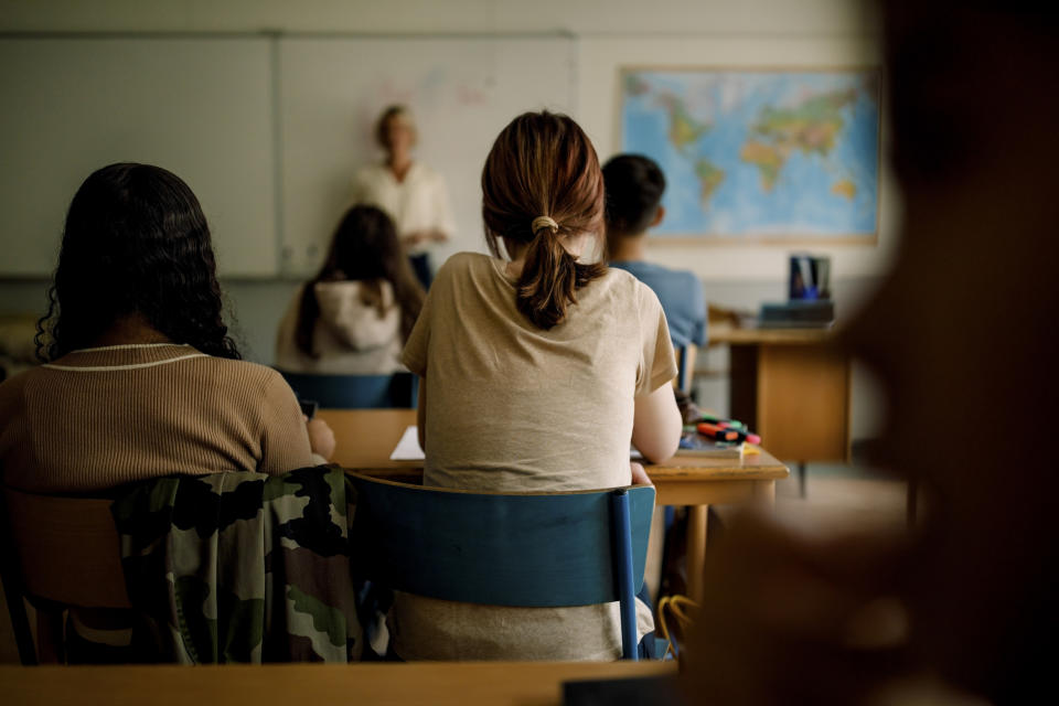 Students seated in a classroom facing a teacher near a world map on the wall