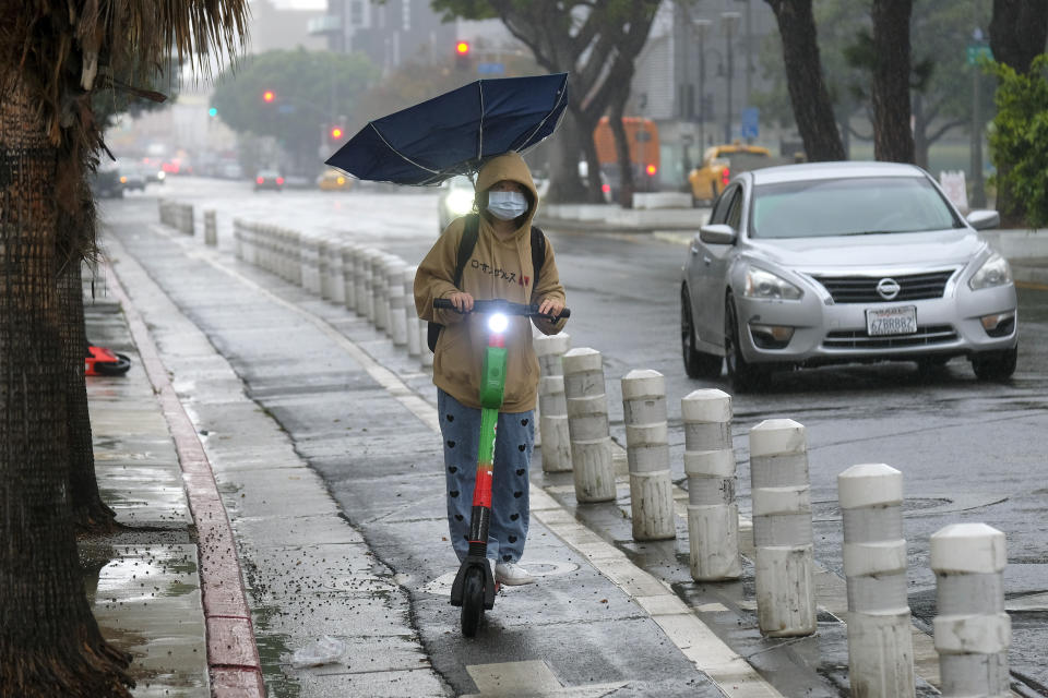 A woman with an umbrella rides her electric scooter through downtown Los Angeles on Thursday, Dec. 23, 2021. (AP Photo/Ringo H.W. Chiu)