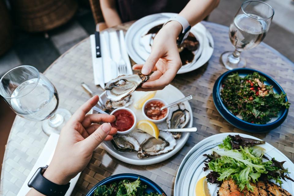 high angle view of woman passing fresh oyster to man across the dining table during lunch, enjoying a scrumptious meal in outdoor restaurant sharing and togetherness eating out lifestyle outdoor dining concept