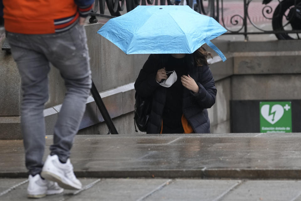 A woman carries her mask to protect against the spread of COVID-19 as she comes out of a subway station in Madrid, Spain, Wednesday, April 20, 2022. Spain is taking another step toward post-pandemic normality by partially ending the obligatory use of masks indoors. A government decree taking effect Wednesday keeps masks still mandatory in medical centers and in all forms of public transport. (AP Photo/Paul White)