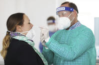 A pharmacist takes a swab from a woman's nose in an adjoining room in Hagen, Germany, Monday, March 8, 2021. The free Corona rapid tests for all citizens were initially only offered by a few pharmacies in North Rhine-Westphalia on the launch day because of many unanswered questions. ( Oliver Berg/dpa via AP)