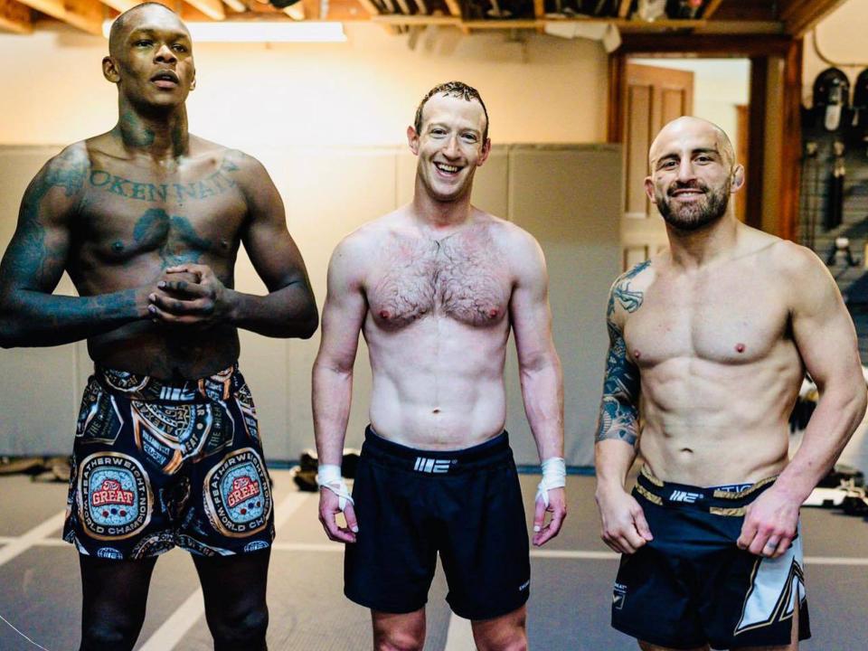 Mark Zuckerberg stands with his shirt off with UFC legends, Israel Adesanya, left, and Alex Volkanovski