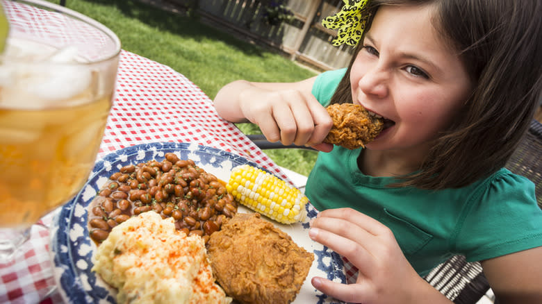 A young girl eating fried chicken at a picnic