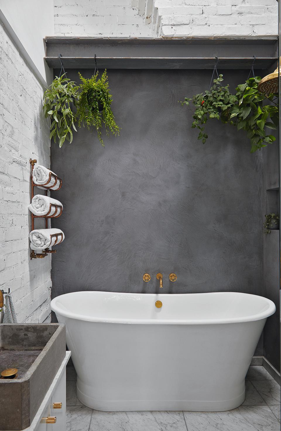 A bathroom with a gray limewash wall, a large bath, and rolled towels in a holder