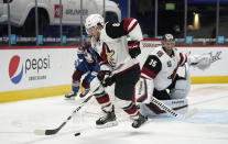 Arizona Coyotes center Nick Schmaltz, front, picks up the puck in front of Coyotes goaltender Darcy Kuemper as Colorado Avalanche right wing Valeri Nichushkin, back, trails the play in the first period of an NHL hockey game Monday, March 8, 2021, in downtown Denver. (AP Photo/David Zalubowski)