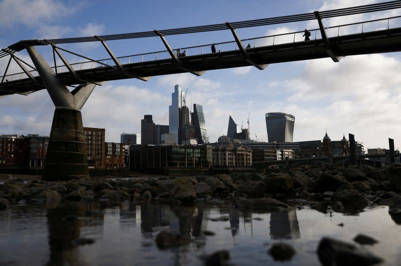FILE PHOTO: The City of London financial district is seen as people walk over Millennium Bridge in London