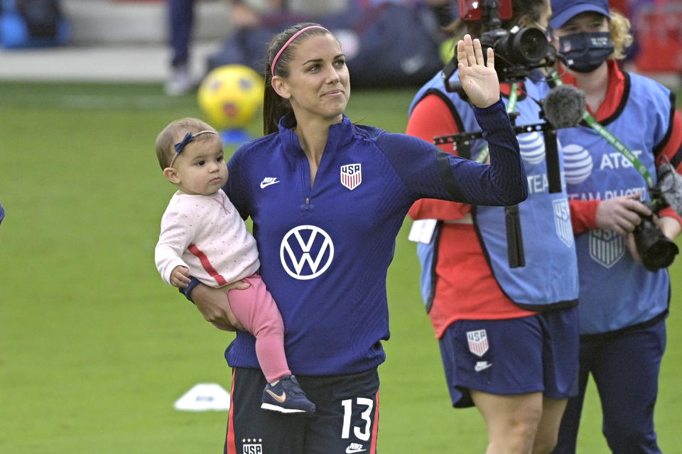 United States forward Alex Morgan (13) waves to fans in the stands while holding her daughter Charlie Elena Carrasco after a SheBelieves Cup women's soccer match against Brazil, Sunday, Feb. 21, 2021, in Orlando, Fla. (AP Photo/Phelan M. Ebenhack)