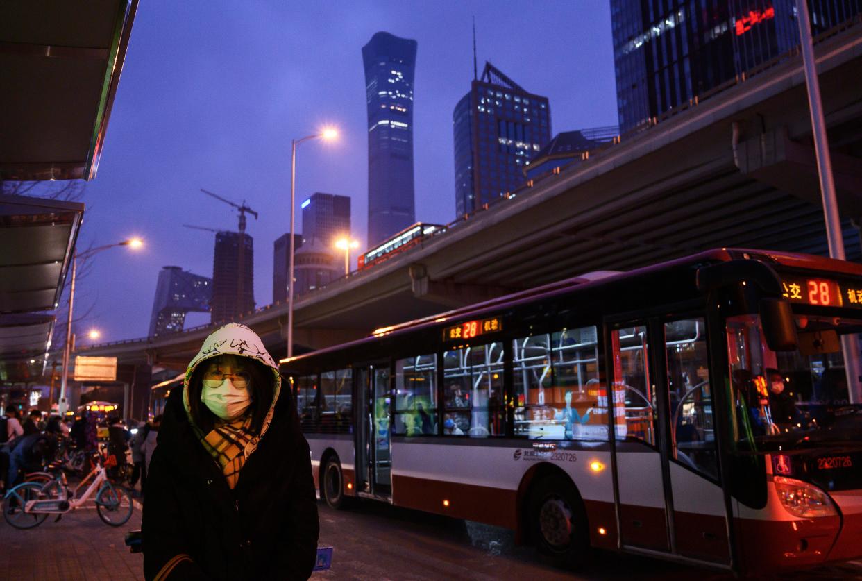 A Chinese office worker wears a protective mask as she waits to take a public bus after leaving work on March 2, 2020 in Beijing, China