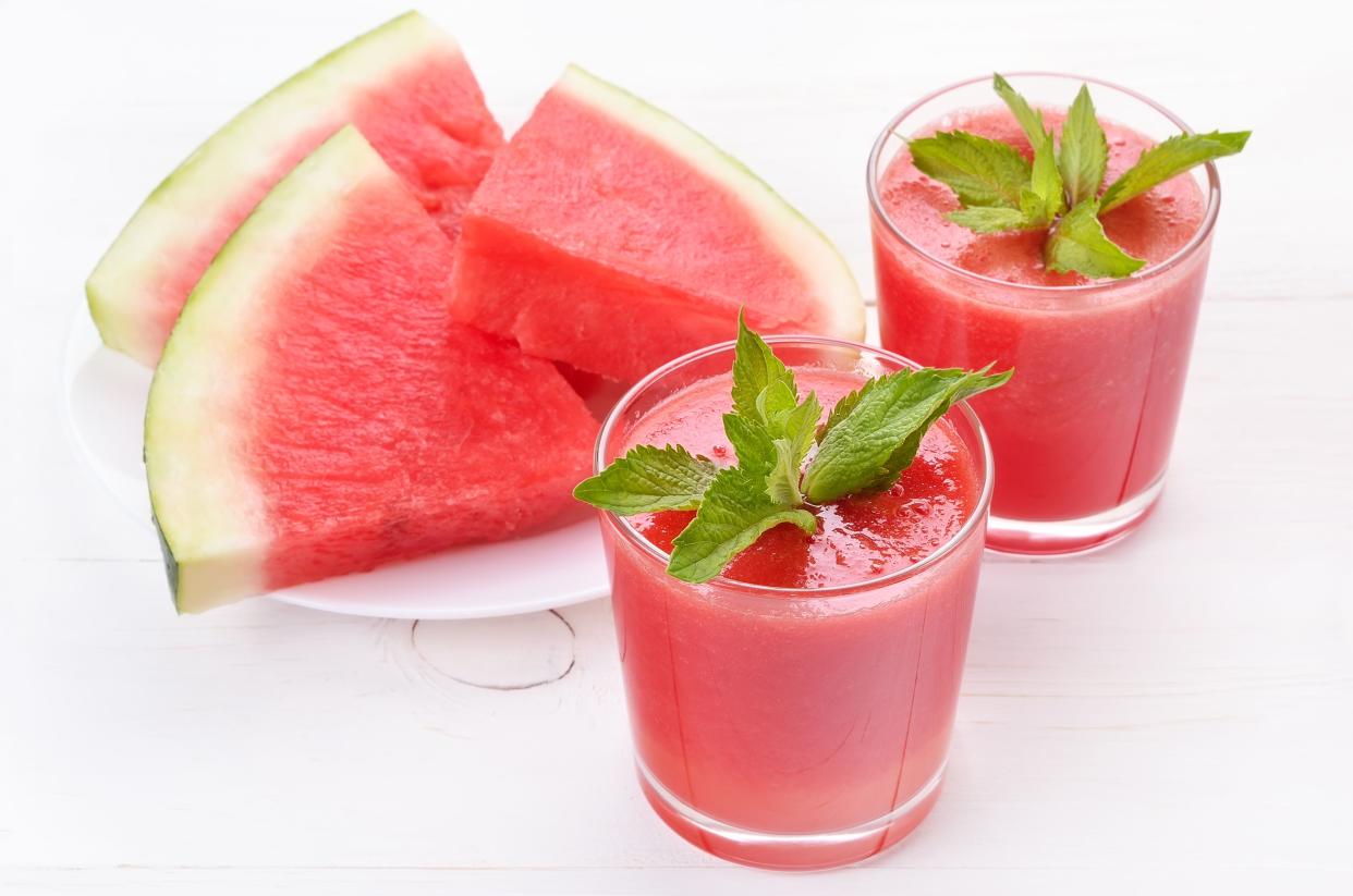 Watermelon cocktail and slices on white wooden table