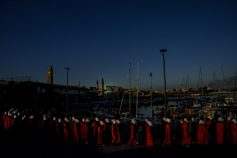 Protesters supporting women's rights dressed as characters from The Handmaid's Tale TV series attend a protest against plans by Prime Minister Benjamin Netanyahu's new government to overhaul the judicial system in the old port of Acre, north Israel, Thursday, March 16, 2023. (AP Photo/Ariel Schalit)