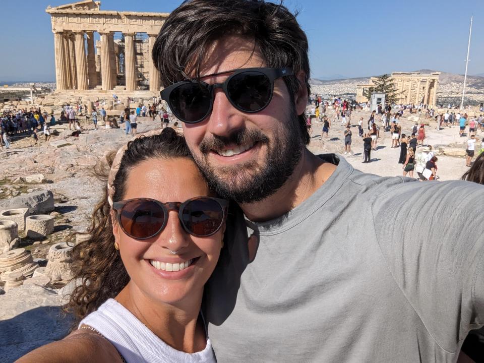The author and her husband smiling in front of the acropolis in greece