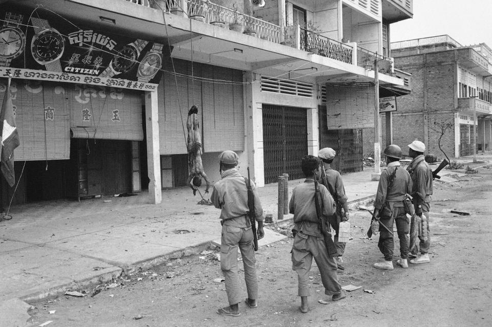 FILE - In this July 6, 1970, file photo, taken by Max Nash, Cambodian soldiers stand by as the body of a slain Viet Cong enemy hangs from a nearby building in the main street of Sanng, south of Phnom Penh. Nash, who covered the conflicts in Southeast Asia and the Middle East and helped nurture a new generation of female photojournalists during more than 40 years with The Associated Press, died Friday, Sept. 28, 2018, after collapsing at home. He was 77. (AP Photo/Max Nash, File)