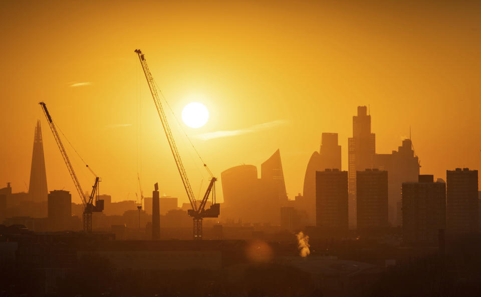 The sun sets behind tower cranes and the London skyline, including the Shard building at left, and other skyscrapers in the city financial district of London, Tuesday Jan. 21, 2020. (Dominic Lipinski/PA via AP)