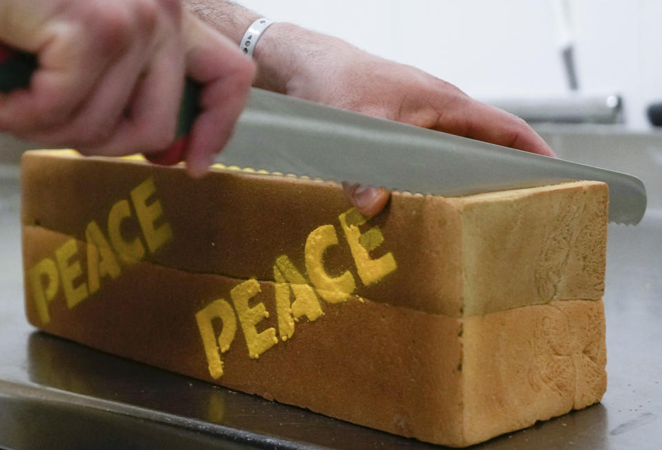 Baker Matteo Cunsolo slices a loaf of 'bread for peace' in his laboratory in Parabiago near Milan in northern Italy, Thursday, March 17, 2022. Cunsolo used saffron and the infusion of a Thai plant to make a bicolor loaf of bread with the colors of the Ukraine national flag and butter-sprayed the word 'peace' on its sides in solidarity with the war-battered country. (AP Photo/Luca Bruno)