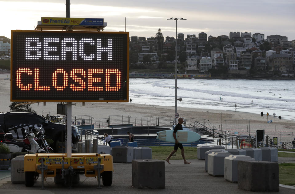 A sign indicates that Bondi Beach is closed as a surfer arrives for the 7 a.m. opening in Sydney, Tuesday, April 28, 2020, as coronavirus pandemic restrictions are eased. The beach is open to swimmers and surfers to exercise only. (AP Photo/Rick Rycroft)