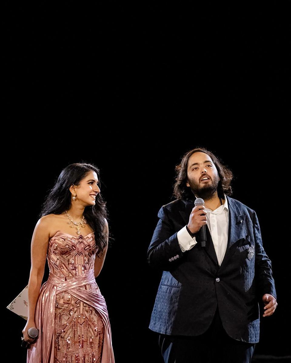 This handout photograph taken and released by Reliance on March 1, 2024, shows director at Reliance's new energy business and Reliance Foundation Anant Ambani (R), son of billionaire tycoon Mukesh Ambani, with his fiancée Radhika Merchant addressing guests during their three-day pre-wedding celebration in Jamnagar.