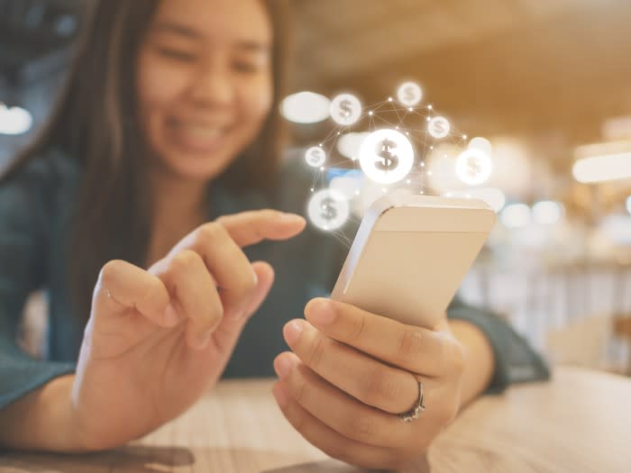 A young girl smiles and uses her smartphone with animations of dollar signs coming out of it.