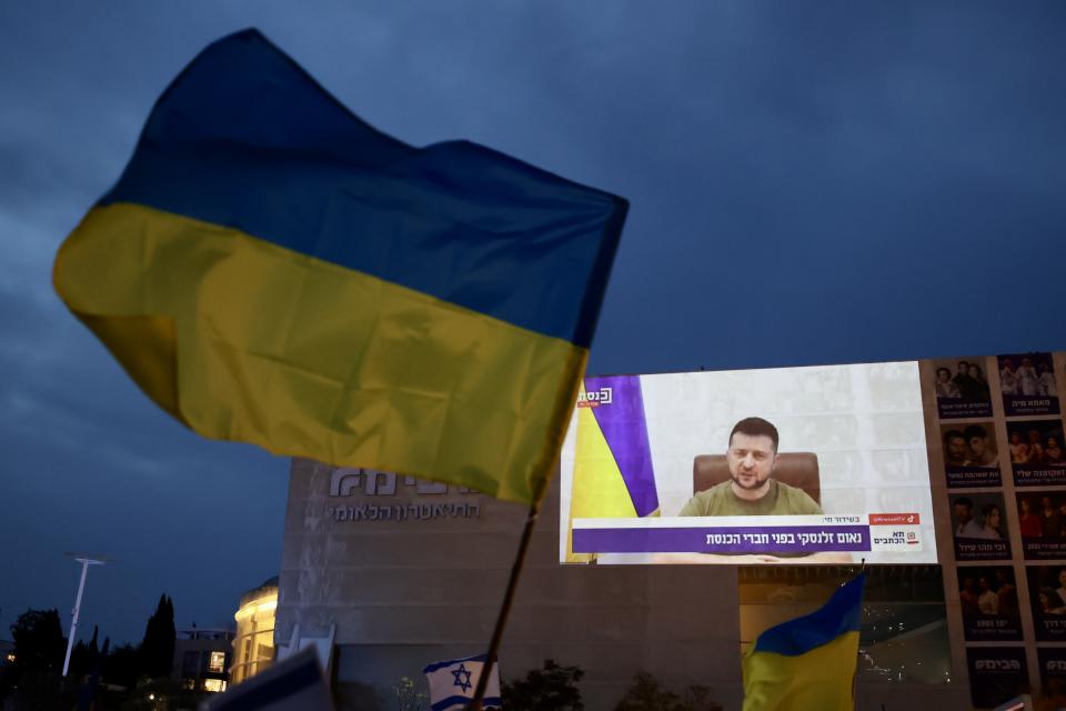 TEL AVIV, ISRAEL - MARCH 20: People, holding banners and flags, are seen during Ukrainian President Volodymyr Zelenskyâs speech on Knesset ( Israelâs parliament) via video conference, in Tel Aviv, Israel on March 20, 2022. A giant screen is set up at Habima Square. (Photo by Mostafa Alkharouf/Anadolu Agency via Getty Images)