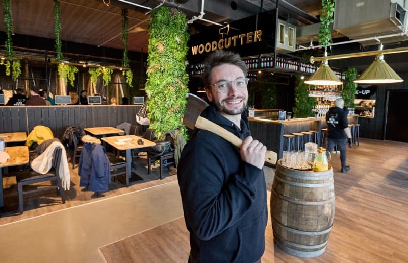 Romain Félix, founder from Belgium, stands with an axe in the WoodCutter axe-throwing bar in Hamburg. Here, patrons swap darts for axes, aiming at wooden targets shaped like tree trunks. Georg Wendt/dpa