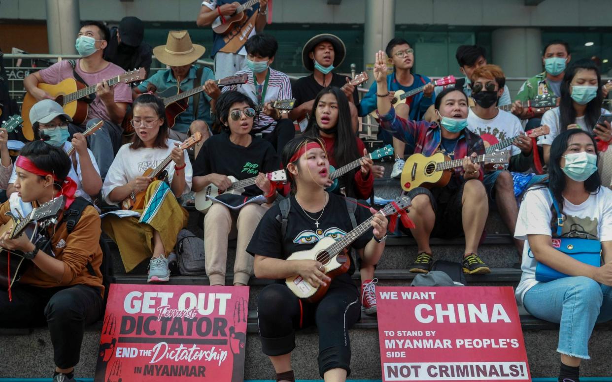 An anti-coup protester flashes the three-fingered salute as others play instruments and sing in Yangon, Myanmar - AP