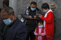 A child wearing a face mask to help curb the spread of the coronavirus looks as masked people browsing their smartphones near Forbidden City in Beijing, Sunday, Oct. 25, 2020. With the outbreak of COVID-19 largely under control within China's borders, the routines of normal daily life have begun to return for its citizens. (AP Photo/Andy Wong)