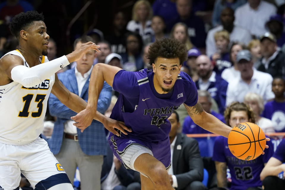 Furman forward Jalen Slawson (20) drives the ball past Chattanooga guard Malachi Smith (13) during an NCAA college basketball championship game for the Southern Conference tournament, Monday, March 7, 2022, in Asheville, N.C. (AP Photo/Kathy Kmonicek)