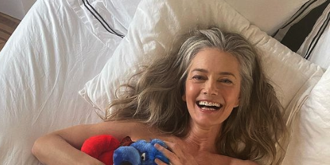 paulina porizkova laying in bed holding a stuffed animal