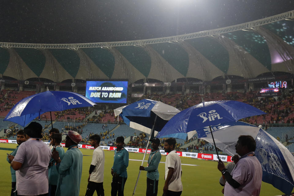 Groundsmen, holding umbrellas, walk in the outfield as an announcement is displayed on a big screen informing spectators after the Indian Premier League cricket match between Lucknow Super Giants and Chennai Super Kings was abandoned due to rains in Lucknow, India, Wednesday, May 3, 2023. (AP Photo/Surjeet Yadav)