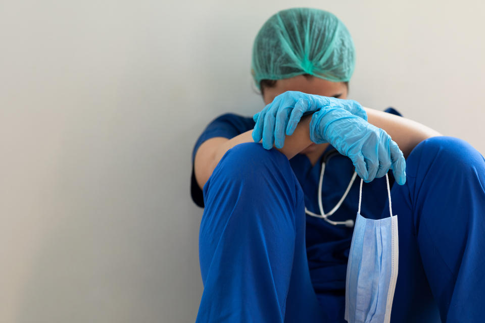 Healthcare worker in scrubs with head down in a moment of fatigue or stress