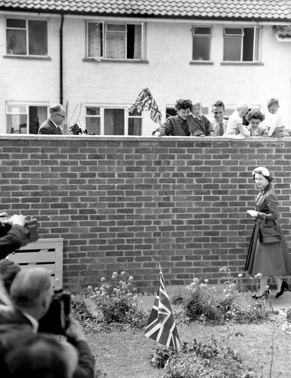Una bandera plantada en el jardín llamó la atención de la reina, que es objeto de la mirada de los vecinos. La vieron llegar para visitar la casa de Eddie Hammond en Crawley New Town, Sussex, después de abrir el aeropuerto de Gatwick, en 1958