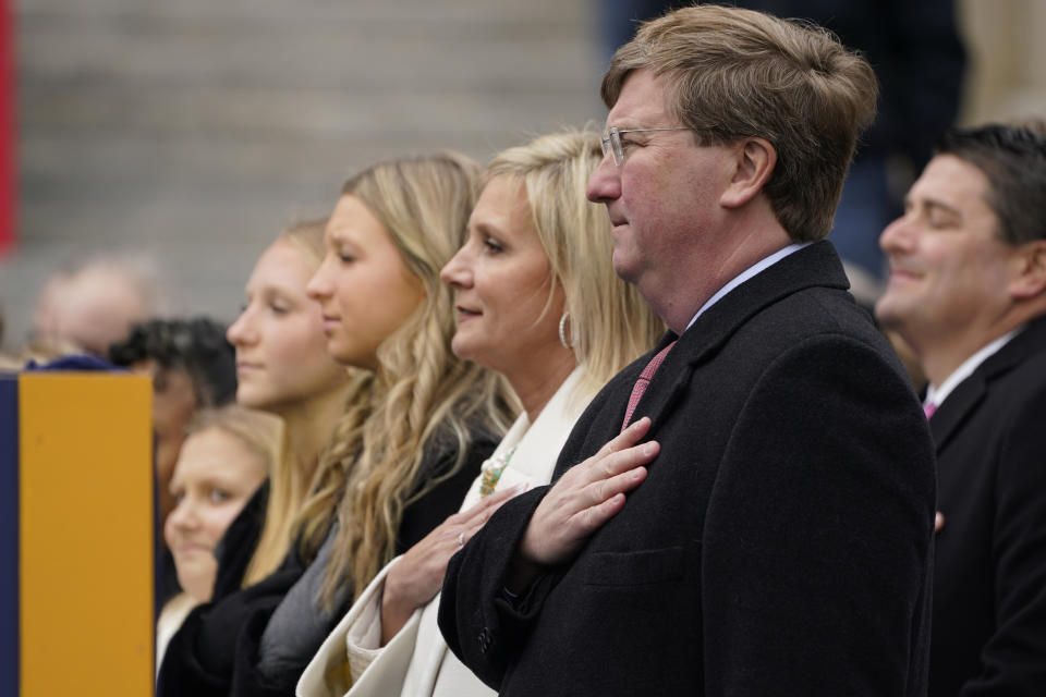 Mississippi Gov. Tate Reeves, right, his wife Elee Reeves, second from right, stand at attention with their daughters during the playing of the National Anthem at the inauguration of the second term for Reeves in Jackson, Miss., Tuesday, Jan. 9, 2024. (AP Photo/Rogelio V. Solis)