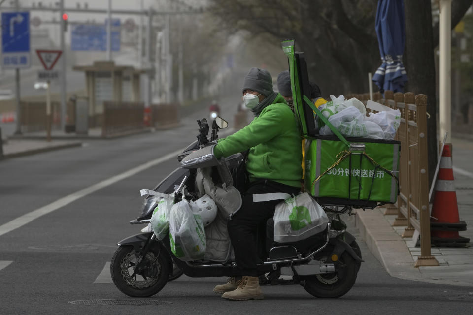 A delivery worker rides on his bike loaded with customers' online order groceries on a street in Beijing, Monday, Dec. 12, 2022. China will drop a travel tracing requirement as part of an uncertain exit from its strict "zero-COVID" policies that have elicited widespread dissatisfaction. (AP Photo/Andy Wong)