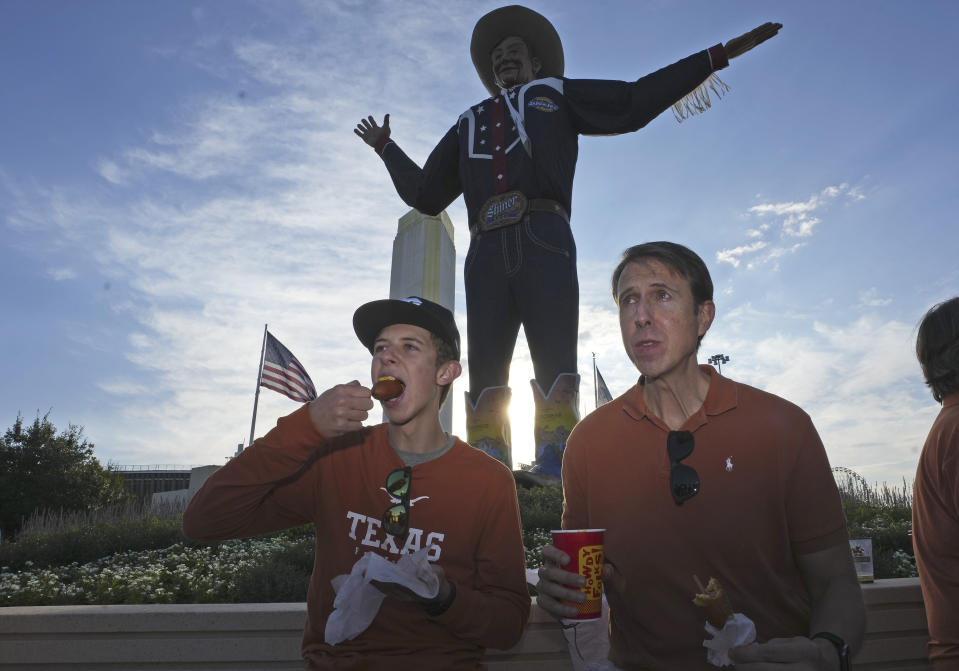 Dennis McGinnis, left, eats a hot corn dog breakfast with his dad Davin McGinnis in front of Big Tex before heading to see an NCAA college football game between Oklahoma and Texas at the Cotton Bowl in Dallas, Saturday, Oct. 7, 2023. (AP Photo/LM Otero)