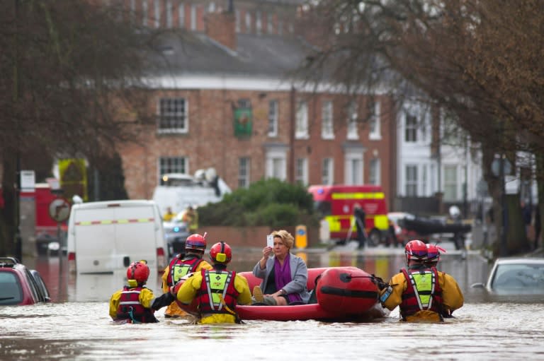 A woman takes a photograph as she is transported to safety by members of the emergency services, after homes were affected by floodwaters in streets in York, northern England