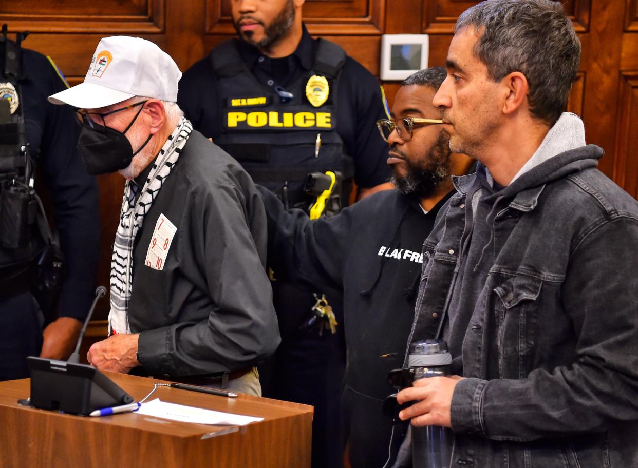 The Rev. John Beaty, left, leaves the council chambers' lectern Monday supported by the Rev. Raymond Greene (center) and Samer Badawi after receiving a warning for violating Akron City Council's public comment rules.