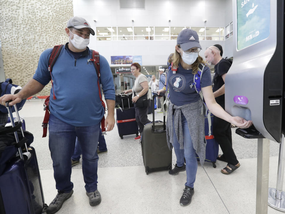 Linda Scruggs, right, applies hand sanitizer as Mike Rustici, left, watches after they arrived on a flight from Lima, Peru, Saturday, March 21, 2020, at Miami International Airport in Miami. The pair's plight illustrates the desperation people stuck abroad experienced as the COVID-19 pandemic spread. Peru confirmed its first case of the virus on March 6. By the time Scruggs and Rustici arrived a week later, it was spreading. (AP Photo/Wilfredo Lee)
