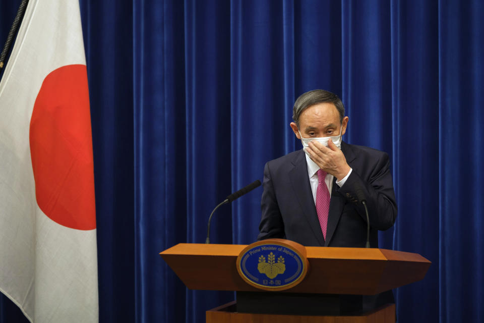 Japan's Prime Minister Yoshihide Suga adjusts a face mask after a press conference on the COVID-19 situation in Japan at the prime minister's office in Tokyo, Friday, Dec. 25, 2020. Suga said on Friday he will seek a legislation to allow the government to impose legally-binding business restriction orders in return for compensation and punish violators as Japan struggles to slow the ongoing upsurge of the coronavirus cases ahead of the holiday season while people are becoming less cooperative. (Nicolas Datiche/Pool Photo via AP)