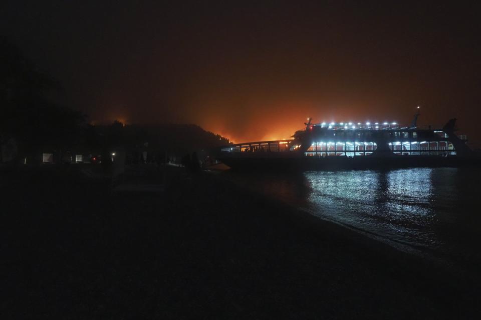 A ferry approaches Kochyli beach to evacuate people near Limni village on the island of Evia, about 160 kilometers (100 miles) north of Athens, Greece, Friday, Aug. 6, 2021. Thousands of people fled wildfires burning out of control in Greece and Turkey on Friday, including a major blaze just north of the Greek capital of Athens that claimed one life, as a protracted heat wave left forests tinder-dry and flames threatened populated areas and electricity installations. (AP Photo/Thodoris Nikolaou)