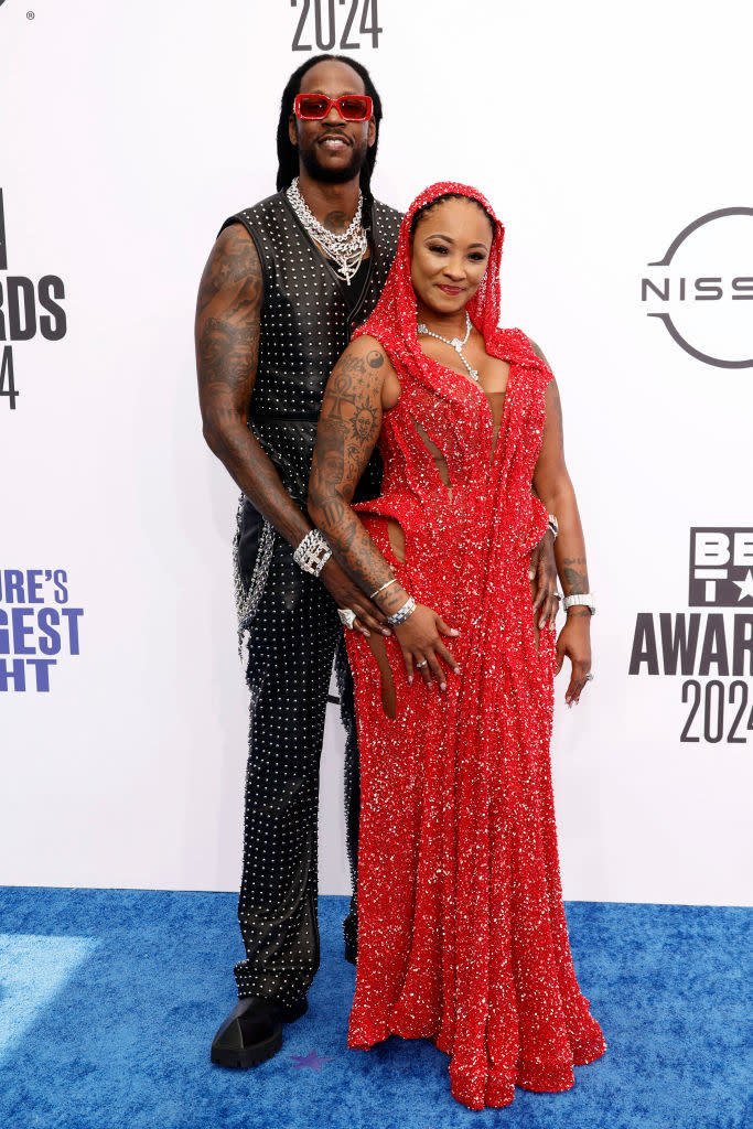 2 Chainz in a black studded vest and pants, and Kesha Ward in a sparkly red gown with a hood, pose together at the BET Awards 2024