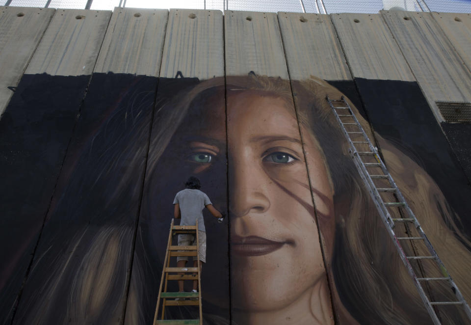 FILE - In this Wednesday, July 25, 2018 file photo, An Artist paints a giant mural of prominent Palestinian activist Ahed Tamimi on part of the Israeli separation wall in the West Bank city of Bethlehem. When Israel locked up Ahed Tamimi for slapping a soldier last year, it hoped to finally silence the teenage Palestinian activist. Instead, it created an international celebrity. (AP Photo/Nasser Nasser, File)