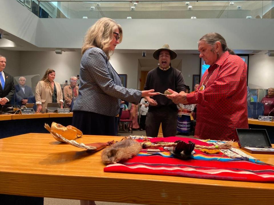 Wolastoq Grand Chief Ron Tremblay presents a wampum belt to Fredericton Mayor Kate Rogers at city hall on Monday, as Juno award-winning singer Jeremy Dutcher performs for the ceremony. (Aidan Cox/CBC - image credit)