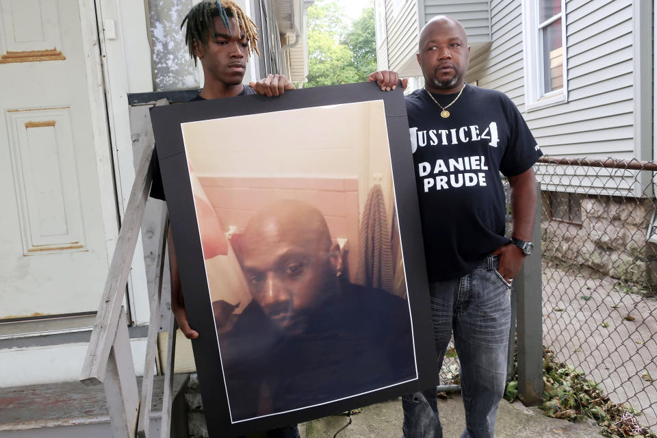 FILE — In this Sept. 3, 2020 file photo, Joe Prude, brother of Daniel Prude, right, and his son Armin, stand with a picture of Daniel Prude in Rochester, N.Y. Newly released transcripts show that a grand jury investigating the police suffocation death of Daniel Prude last year in Rochester, New York, voted 15-5 to clear the three officers involved in his restraint of a criminally negligent homicide charge sought by prosecutors. (AP Photo/Ted Shaffrey, File)