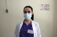 In this photo taken on Friday, May 8, 2020, medical student Anna Karagiannakou poses for a photo at the entrance of the COVID-19 Clinic at Sotiria Hospital in Athens. Greece's main hospital for the treatment of COVID-19 is also the focus of a hands-on training program for dozens of medical students who volunteered to relieve hard-pressed doctors from their simpler duties while gaining a close peek at the front lines of a struggle unmatched in modern medical history. The sign below, placed above a box that has since been removed, reads ''This is where you leave your complaints, your suggestions and your congratulations too.'' (AP Photo/Thanassis Stavrakis)
