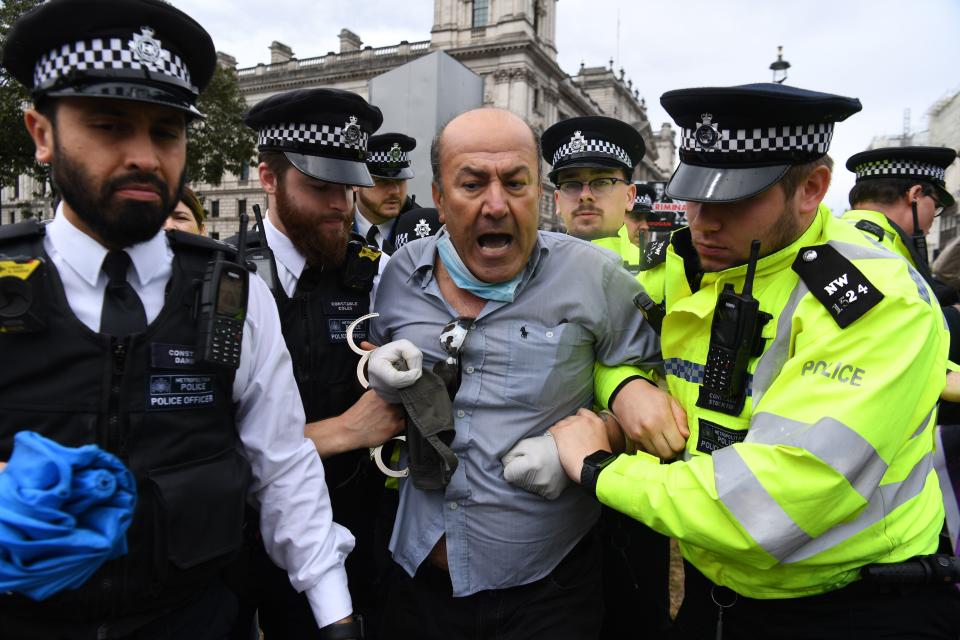 A pro-Kurdish protester who ran into the road toward the car of Britain's Prime Minister Boris Johnson as it was leaving the Houses of Parliament in London on June 17, 2020 is led away by police officers. - The protester ran into the road towards the Jaguar that normally carries the Prime Minister Boris Johnson and was stopped by police. As the Jaguar stopped it was subsequently struck from behind by the next vehicle in the convoy resulting in a large dent. (Photo by DANIEL LEAL-OLIVAS / AFP) (Photo by DANIEL LEAL-OLIVAS/AFP via Getty Images)